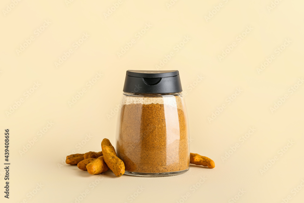 Jar of turmeric powder and roots on color background