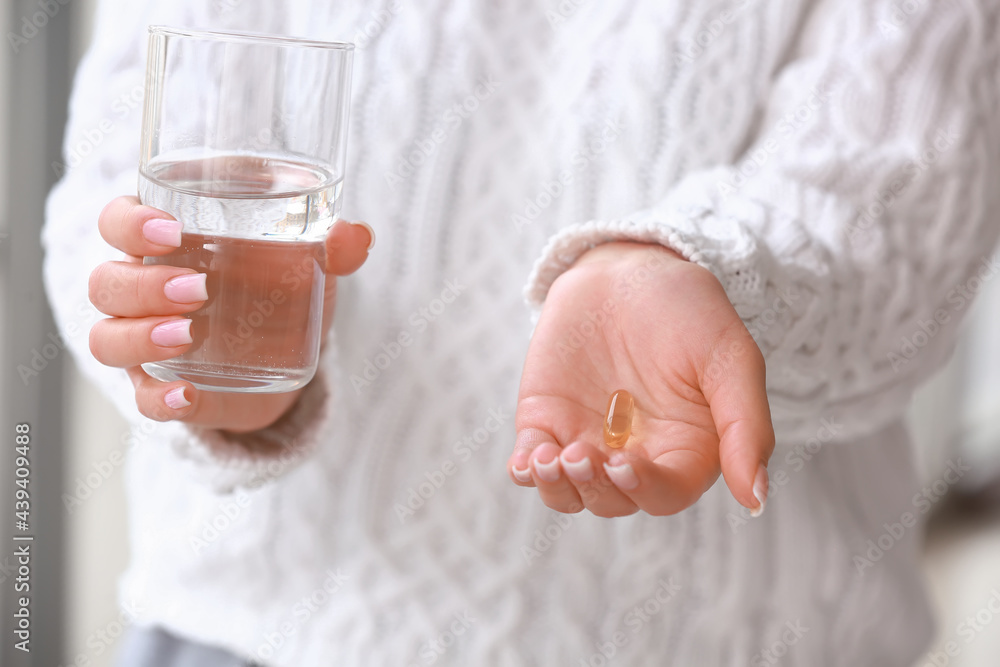 Young woman with fish oil pill at home, closeup