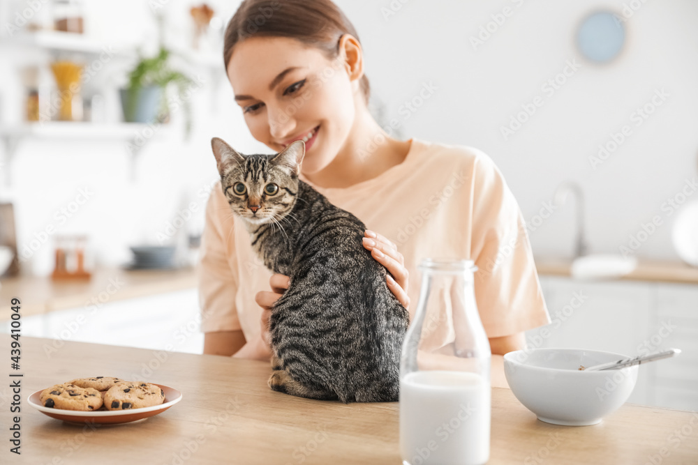 Beautiful young woman with cute cat in kitchen