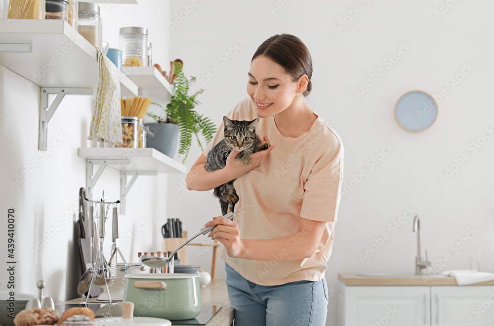 美丽的年轻女人和可爱的猫在厨房做饭