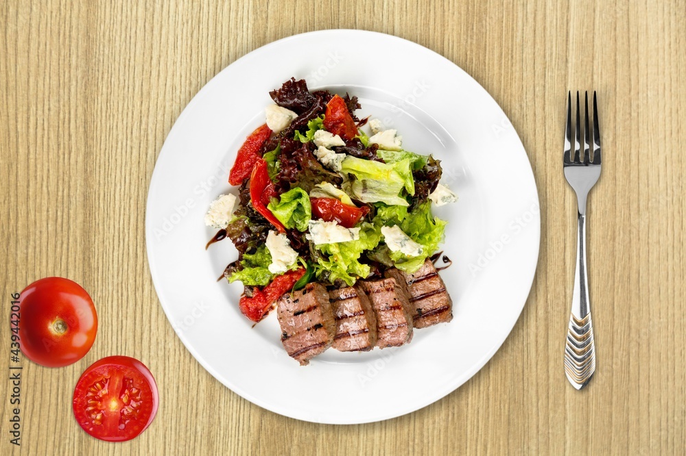 White plate of chicken salad with vegetables on a wooden table