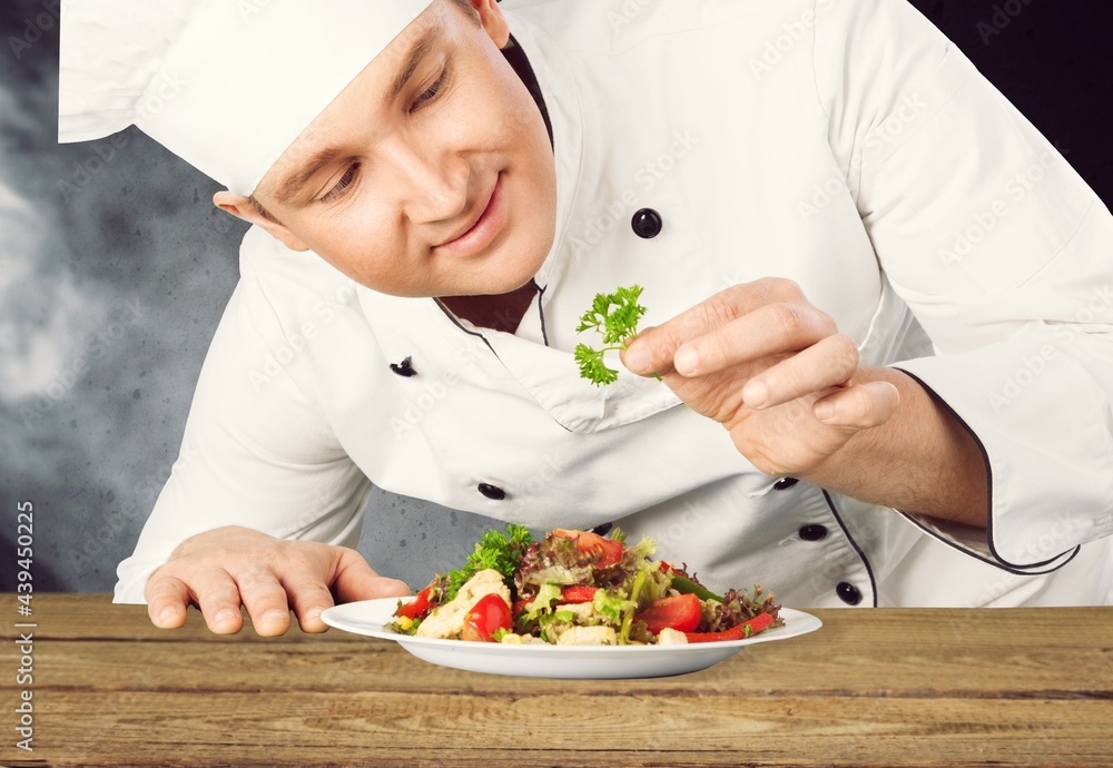 Male chef dressing dish with fresh greens before it is going to be served for restaurant guests