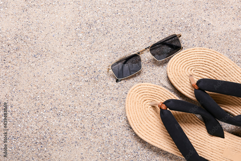 Stylish sunglasses with flip-flops on sand