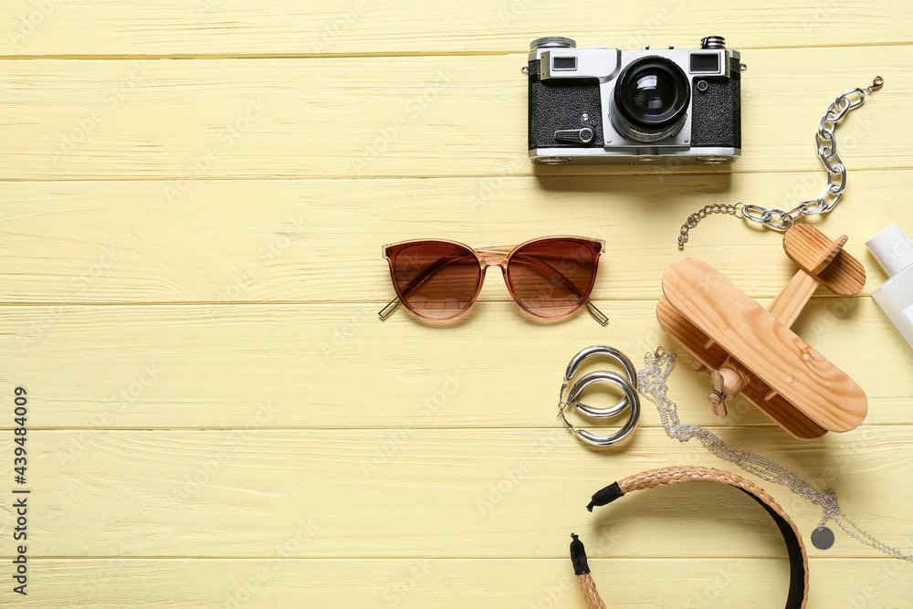 Stylish female accessories with photo camera and airplane on color wooden background