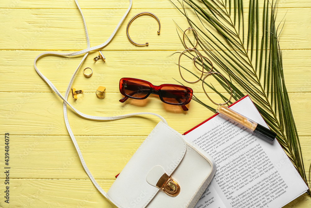 Stylish female accessories with book on color wooden background