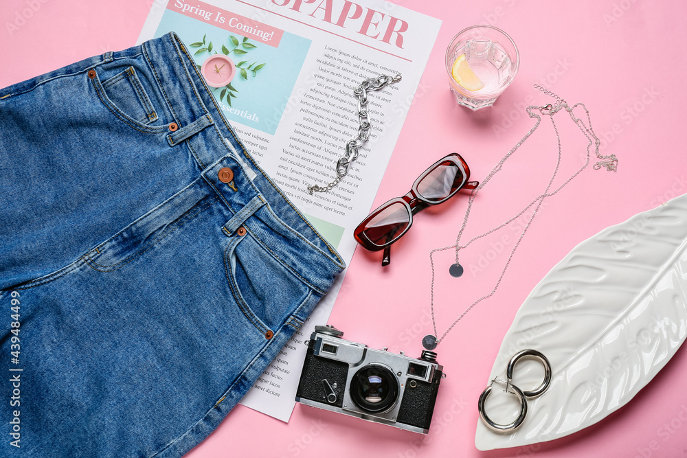 Stylish female accessories with jeans pants, newspaper and photo camera on color background