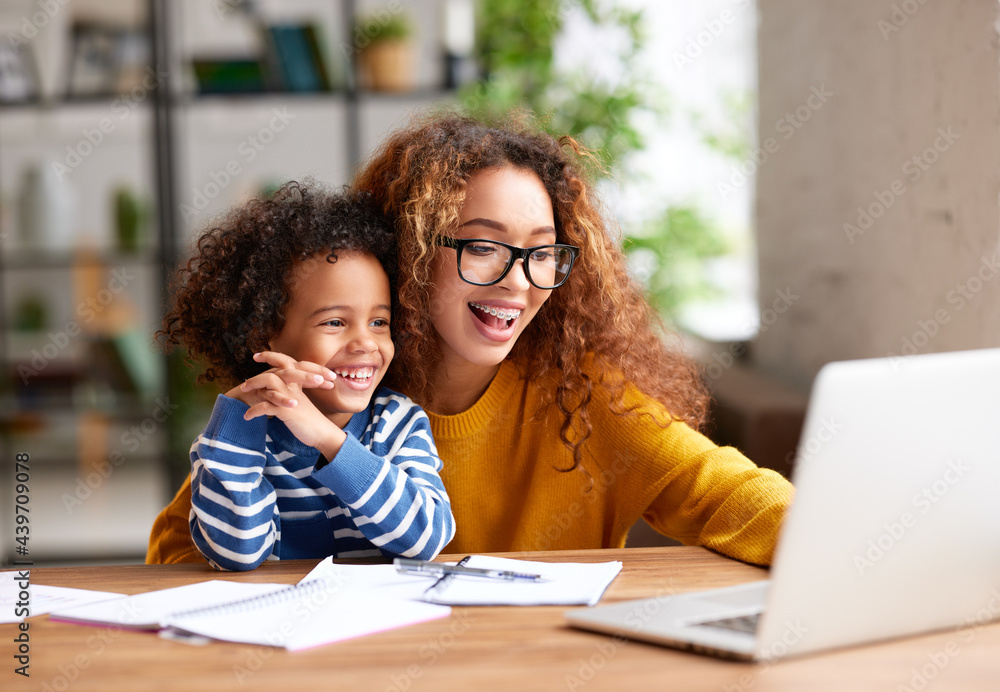 Happy afro american family mom and son watching funny videos on laptop at home