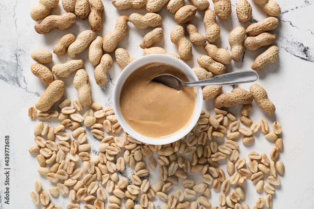 Bowl with tasty peanut butter and nuts on white background