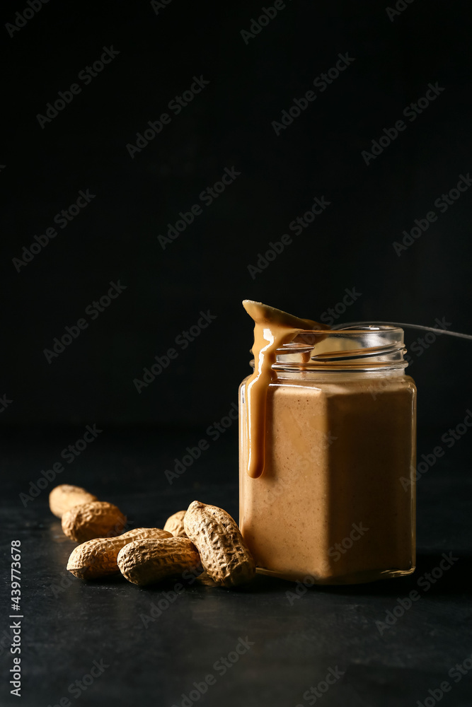 Jar with tasty peanut butter on dark background