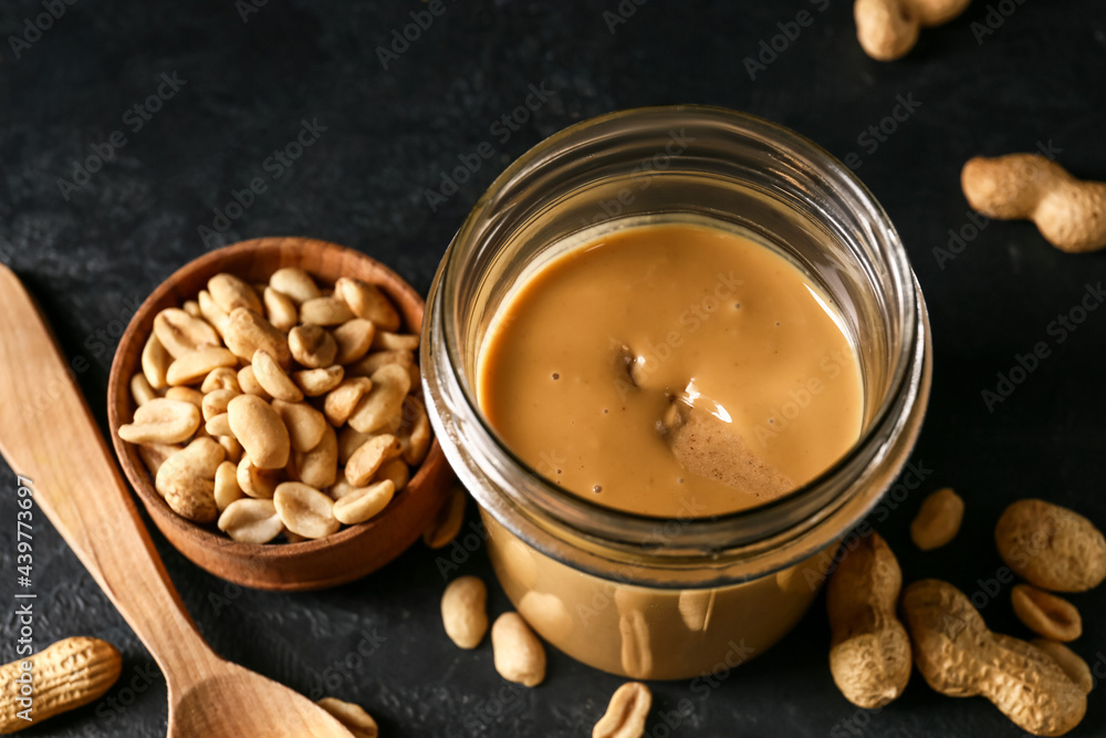 Jar with tasty peanut butter on dark background