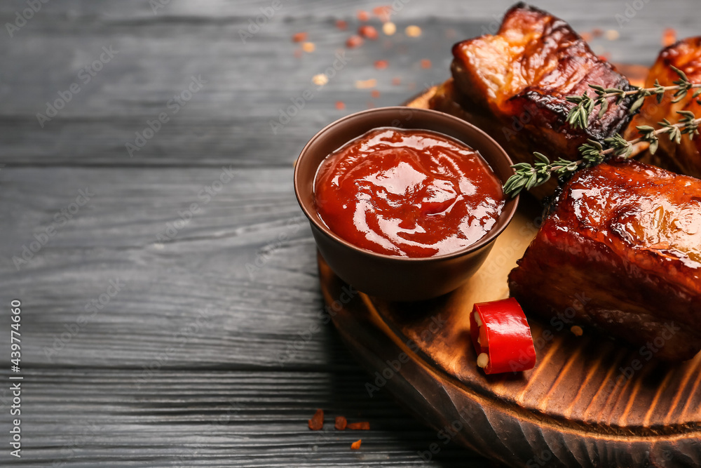 Board with tasty barbecue sauce and grilled pork on dark wooden background