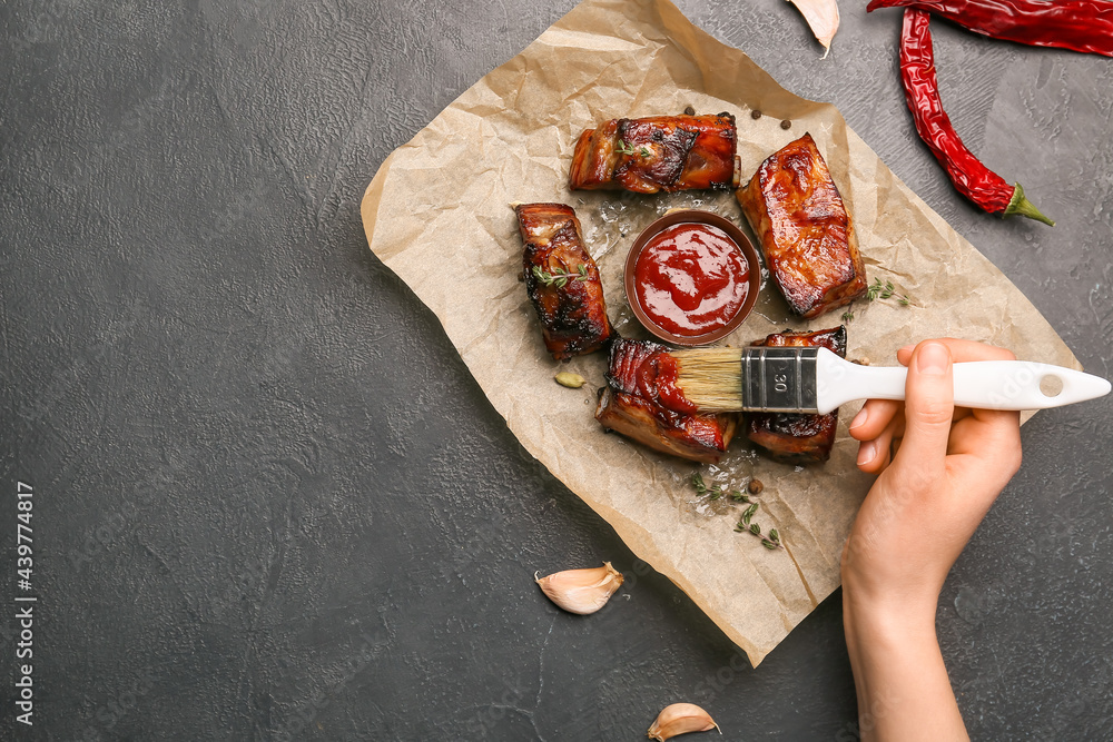 Woman spreading barbecue sauce on roasted pork on dark background