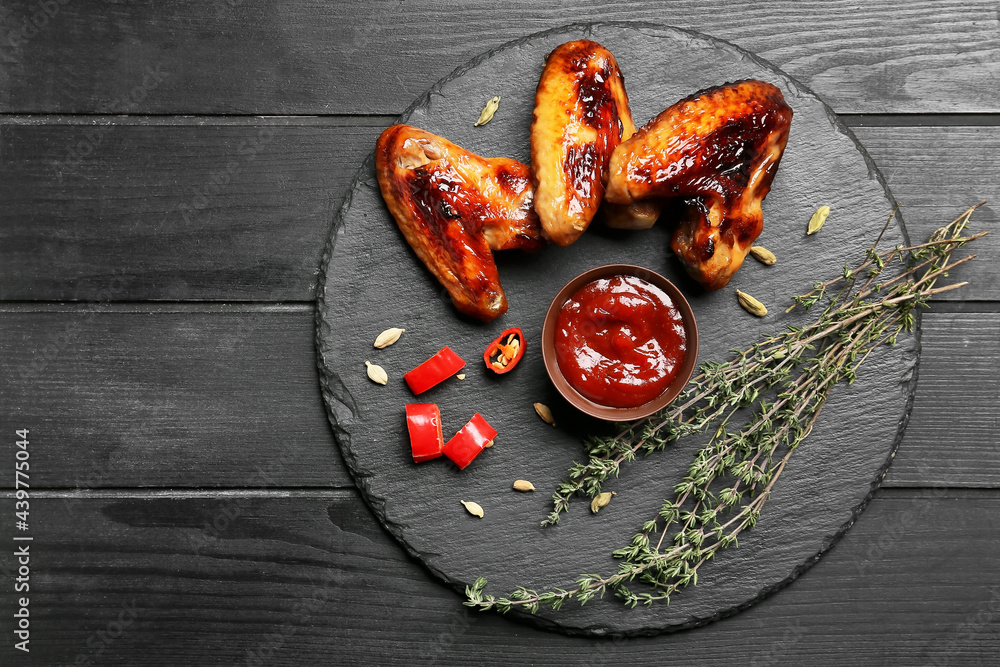 Board with roasted chicken wings and barbecue sauce on dark wooden background