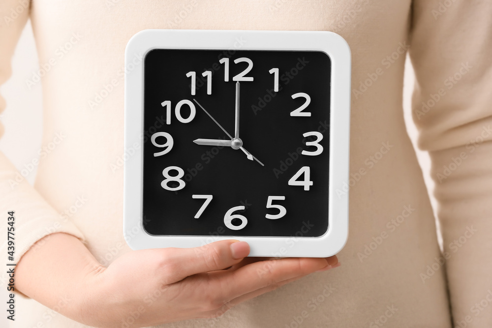 Young woman with alarm clock on light background, closeup