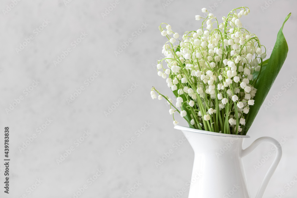 Jug with beautiful lily-of-the-valley flowers on light background