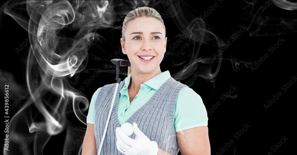 Caucasian female golf player holding golf club and ball against smoke effect on black background