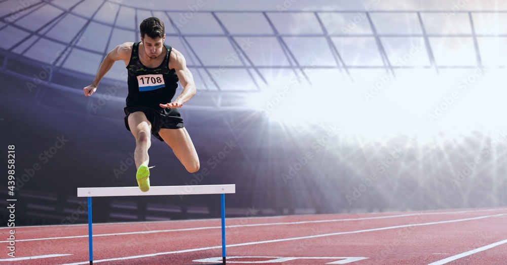 Caucasian male athlete jumping over a hurdle against sports field in background