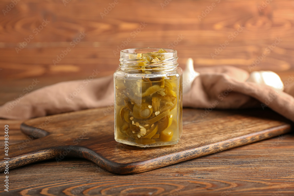 Glass jar with canned jalapeno on wooden background