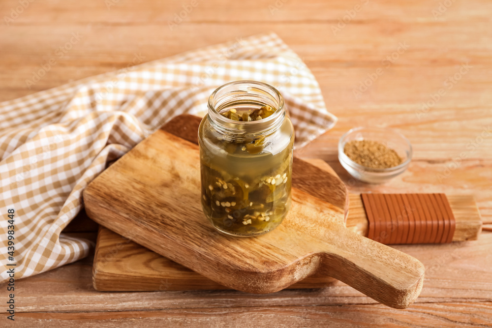 Glass jar with canned jalapeno on wooden background