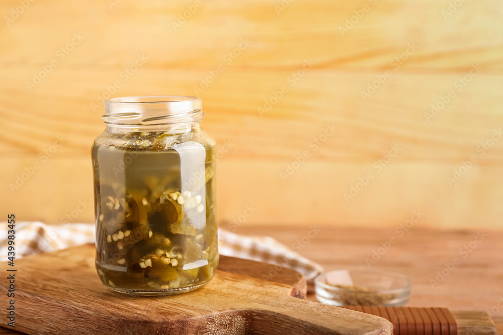 Glass jar with canned jalapeno on wooden background