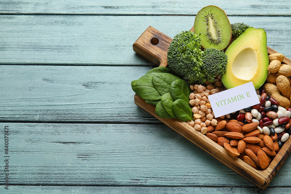 Board with healthy products rich in vitamin E on color wooden background