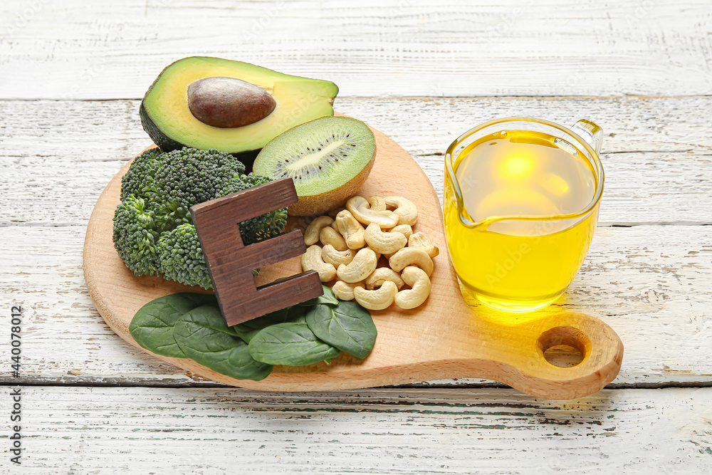 Board with healthy products rich in vitamin E on light wooden background