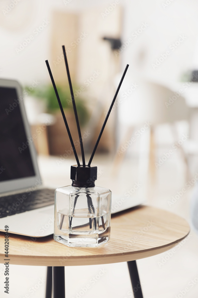 Reed diffuser with laptop on table in room, closeup