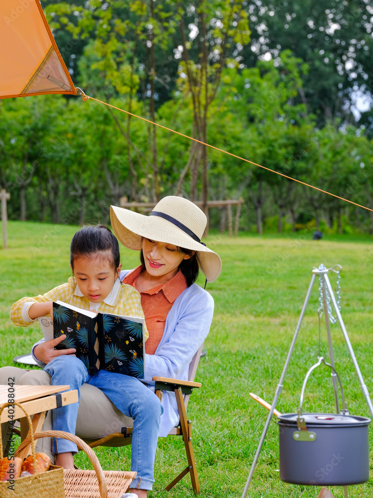 Happy mother and daughter sitting outside reading