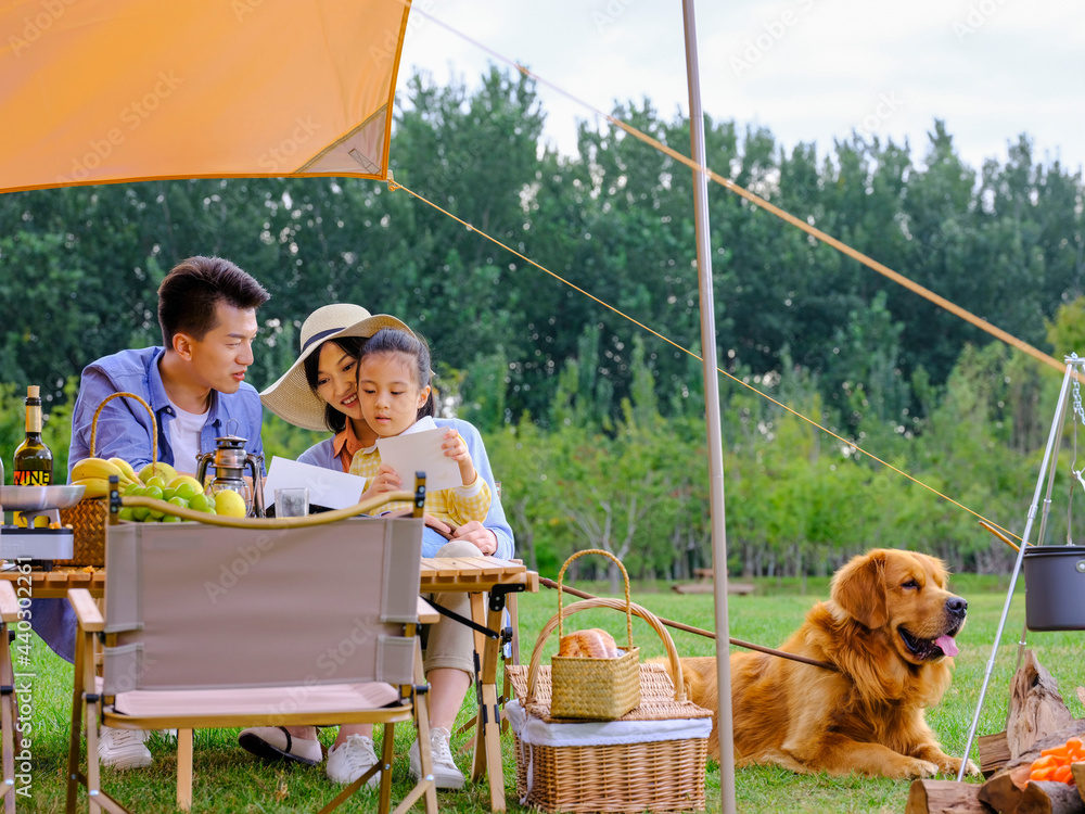 Happy family of three and pet dog reading outside