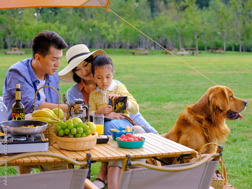 Happy family of three and pet dog reading outside