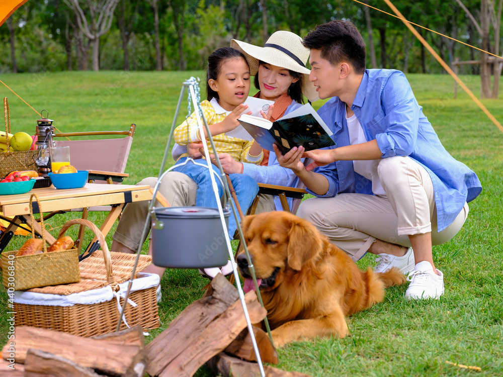 Happy family of three and pet dog reading outside