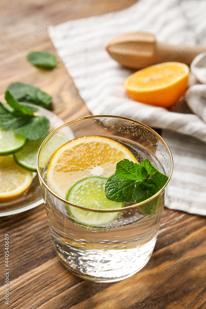 Glass of healthy lemonade and citrus fruits on wooden background