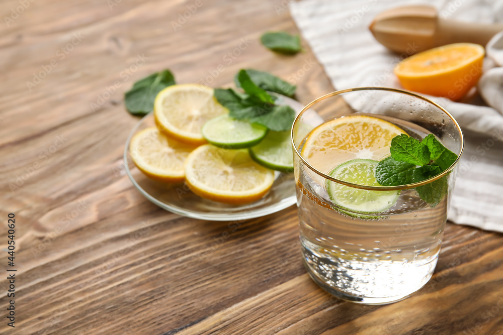 Glass of healthy lemonade and citrus fruits on wooden background