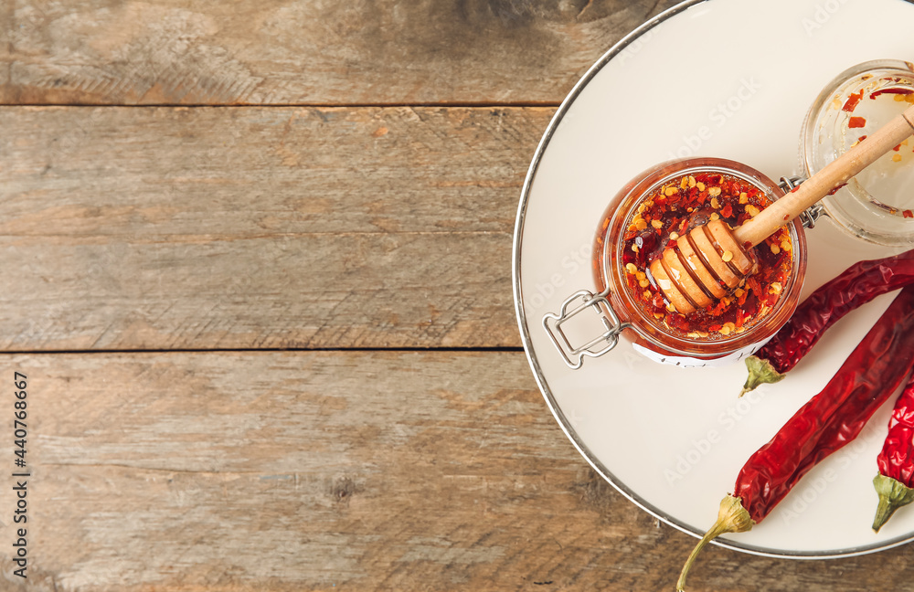 Plate with hot honey and chili peppers on wooden background