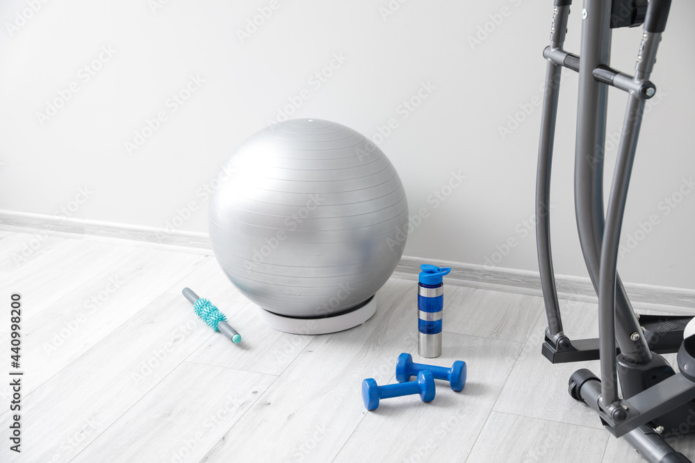 Different sports equipment with fitness ball near light wall