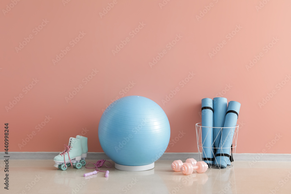 Set of sports equipment with fitness ball and roller skates on color background