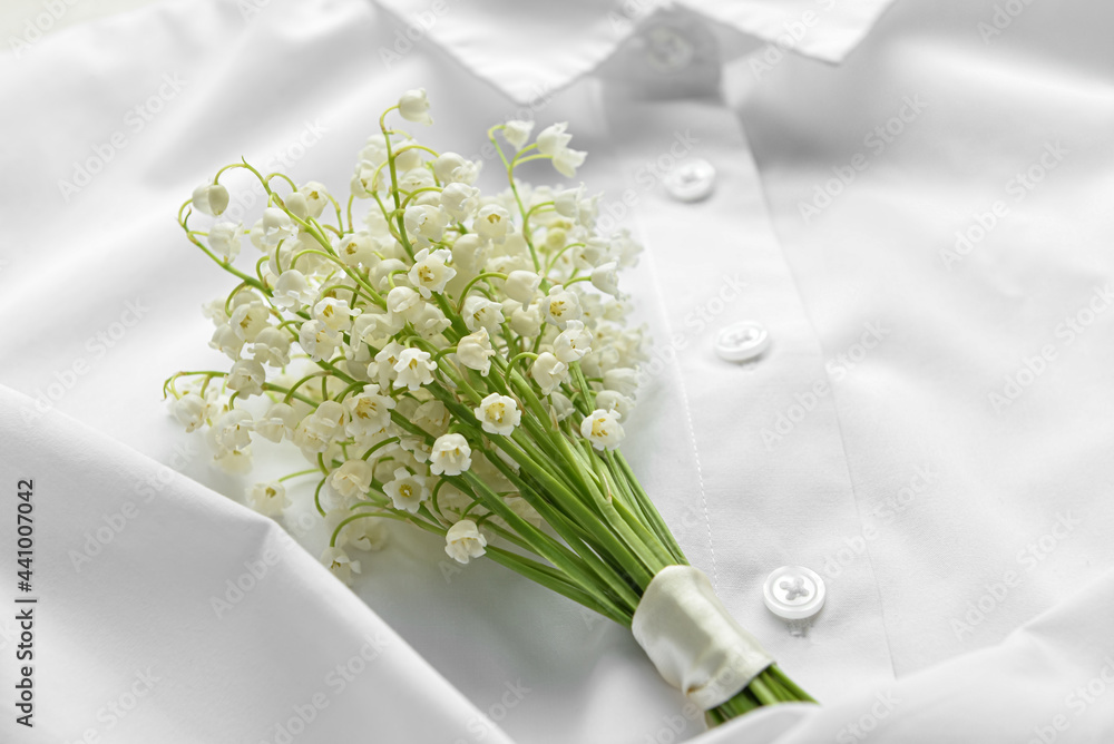 Beautiful lily-of-the-valley flowers on white shirt, closeup