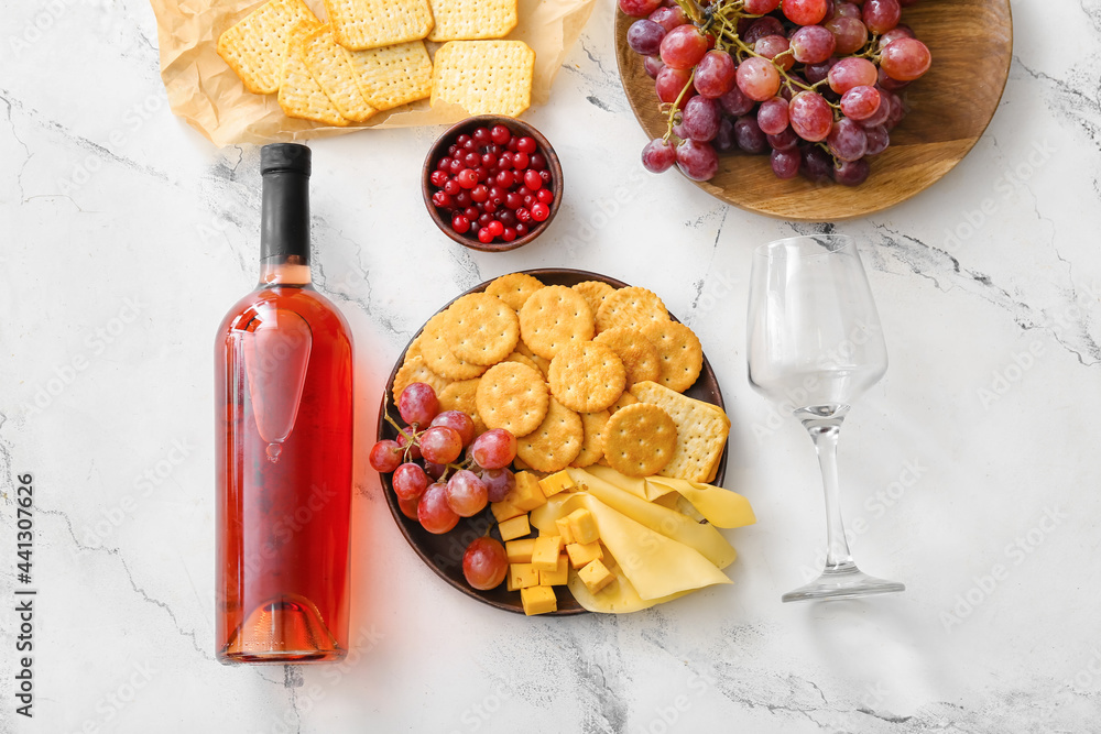 Plate with tasty crackers with cheese, bottle of wine and snacks on light background