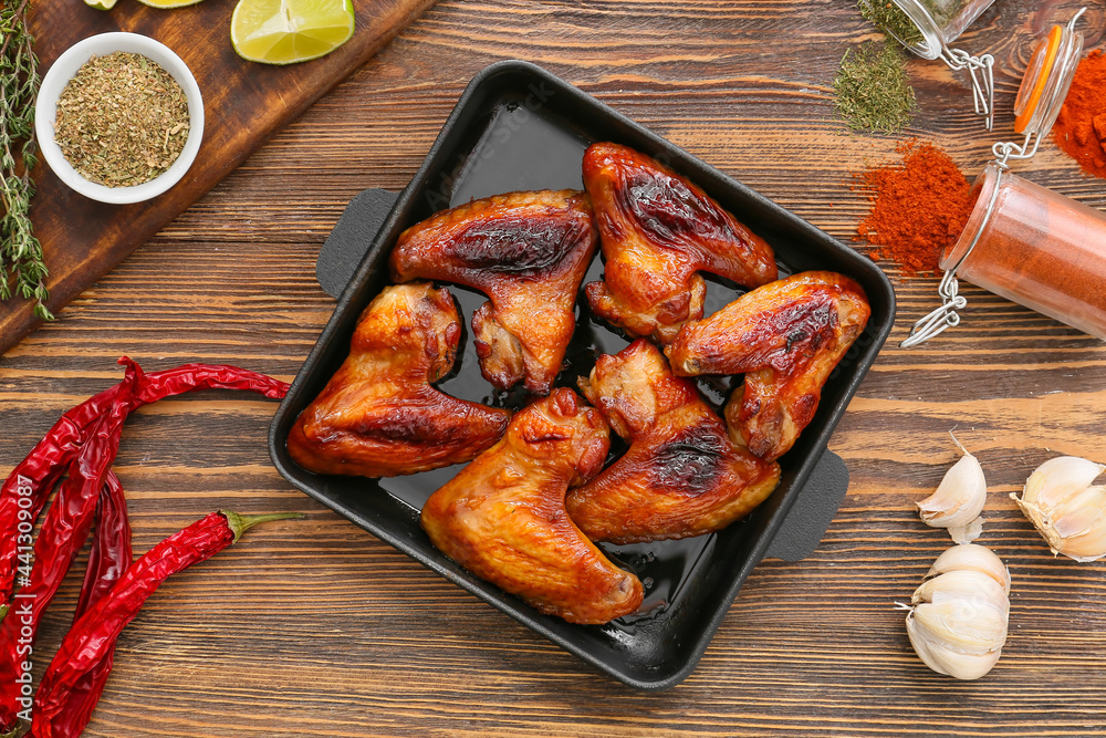 Baking dish with roasted chicken wings on wooden background