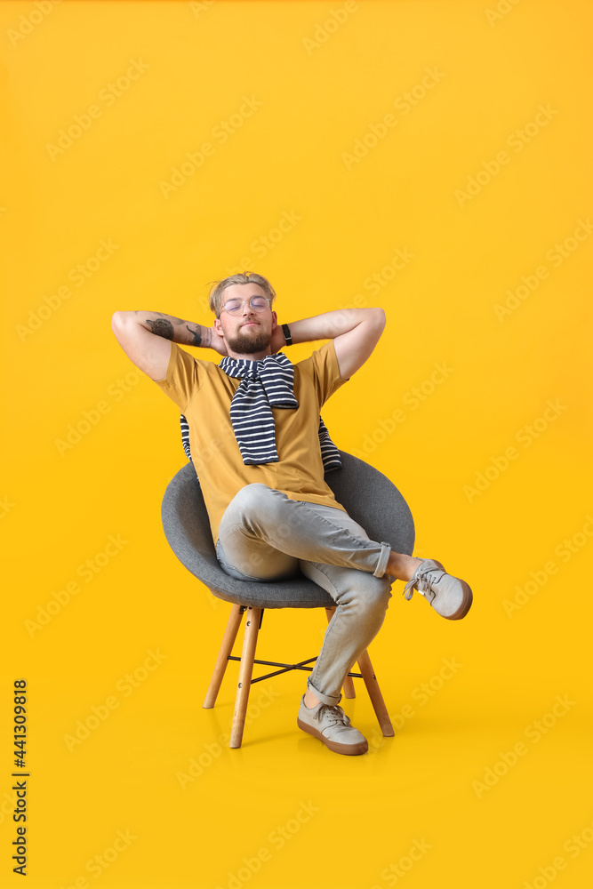 Handsome young man sitting in armchair on color background