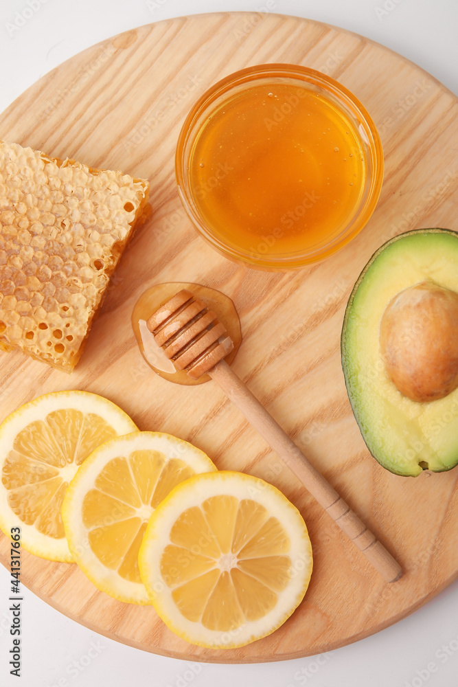 Glass bowl with sweet honey, lemon slices, comb and avocado on white background