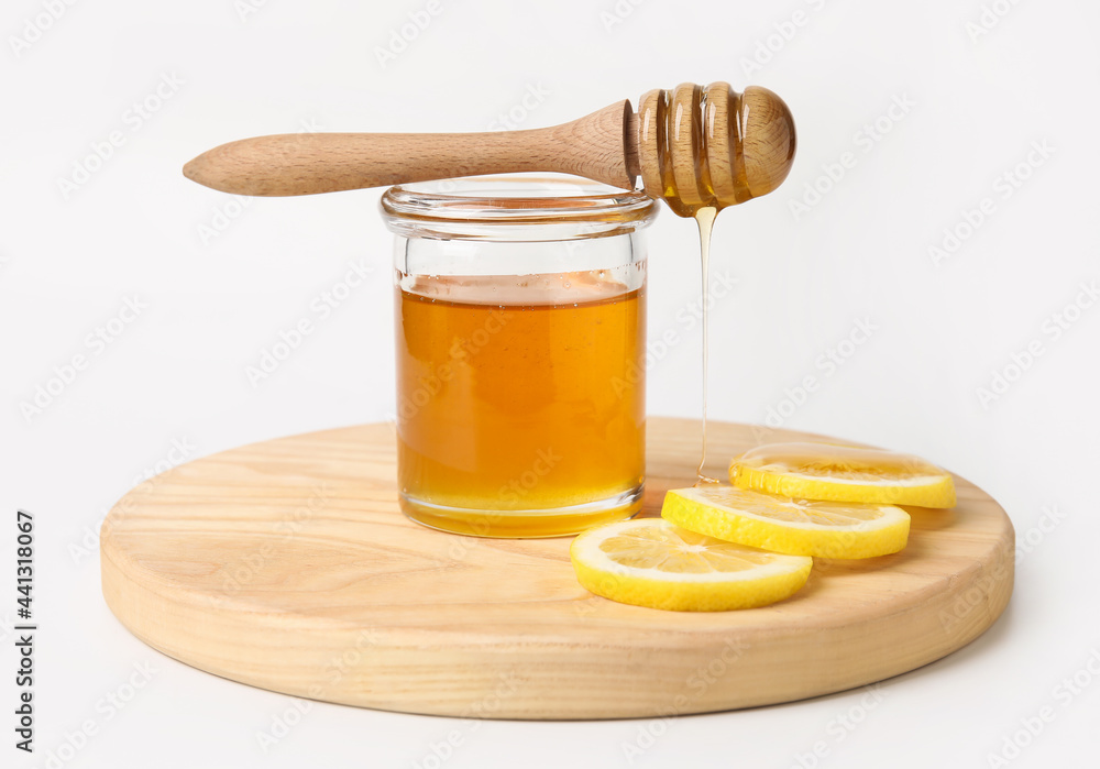 Glass jar with sweet honey, dipper and lemon slices on white background