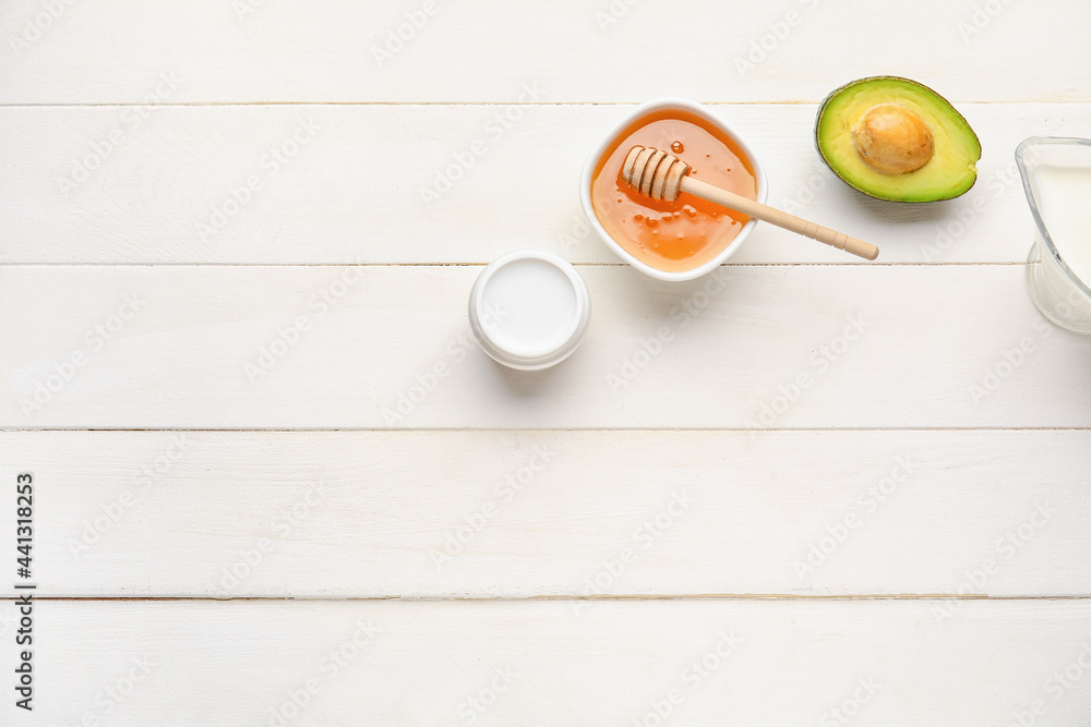 Bowl with sweet honey, avocado, jug of milk and cosmetic product on light wooden background