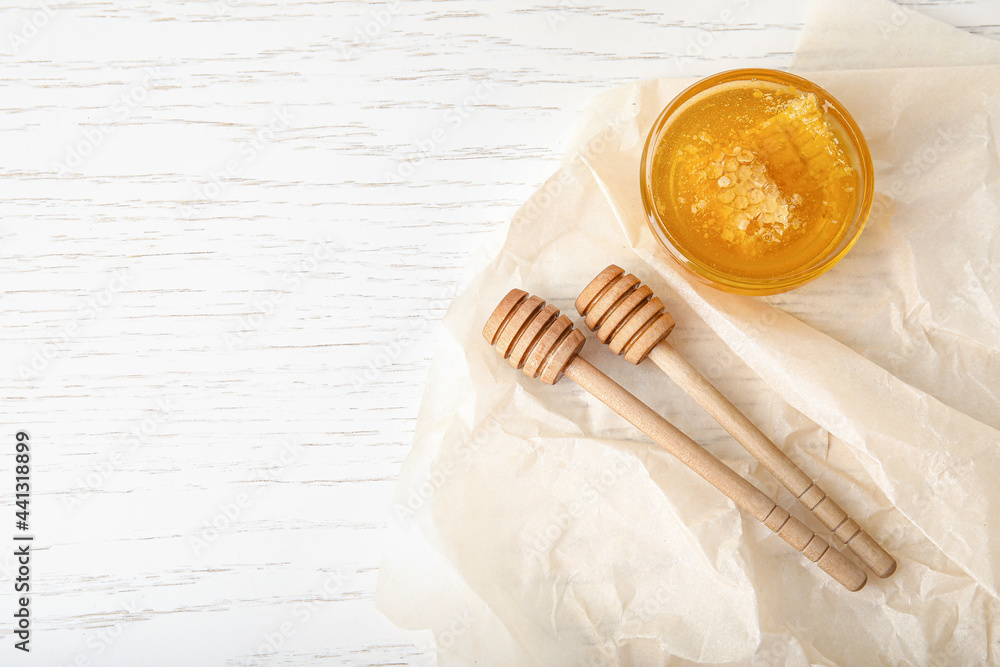 Glass bowl with sweet honey and dippers on light wooden background