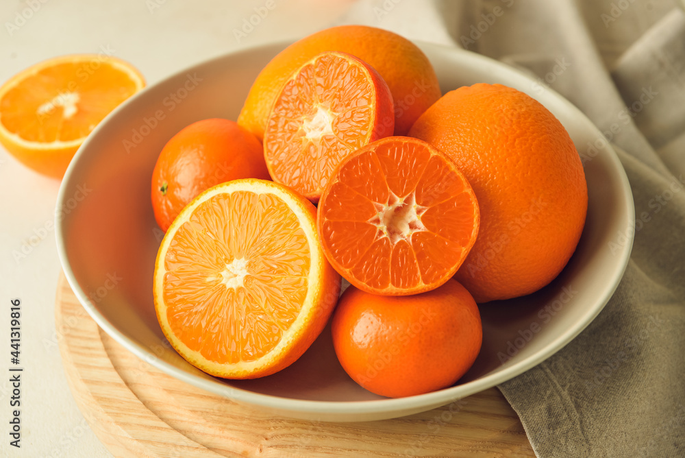 Plate with healthy oranges and tangerines on light background