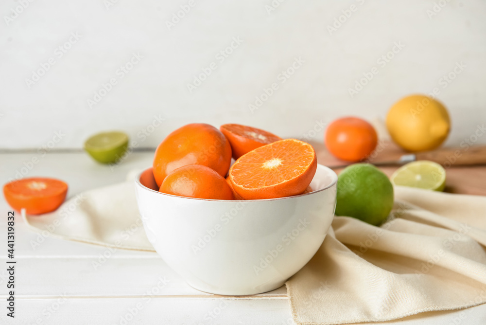 Bowl with healthy citrus fruits on light wooden background