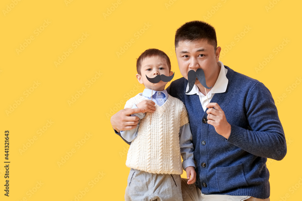 Happy father and his little son with party decor on color background