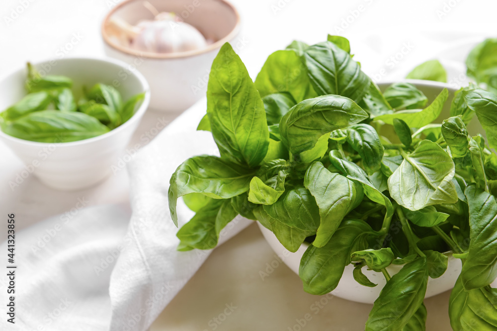 Bowl with fresh basil leaves on light background