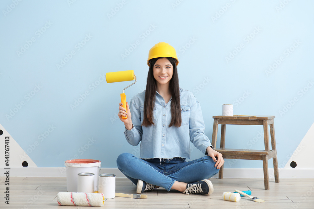 Young woman with roller and cans of paint near color wall