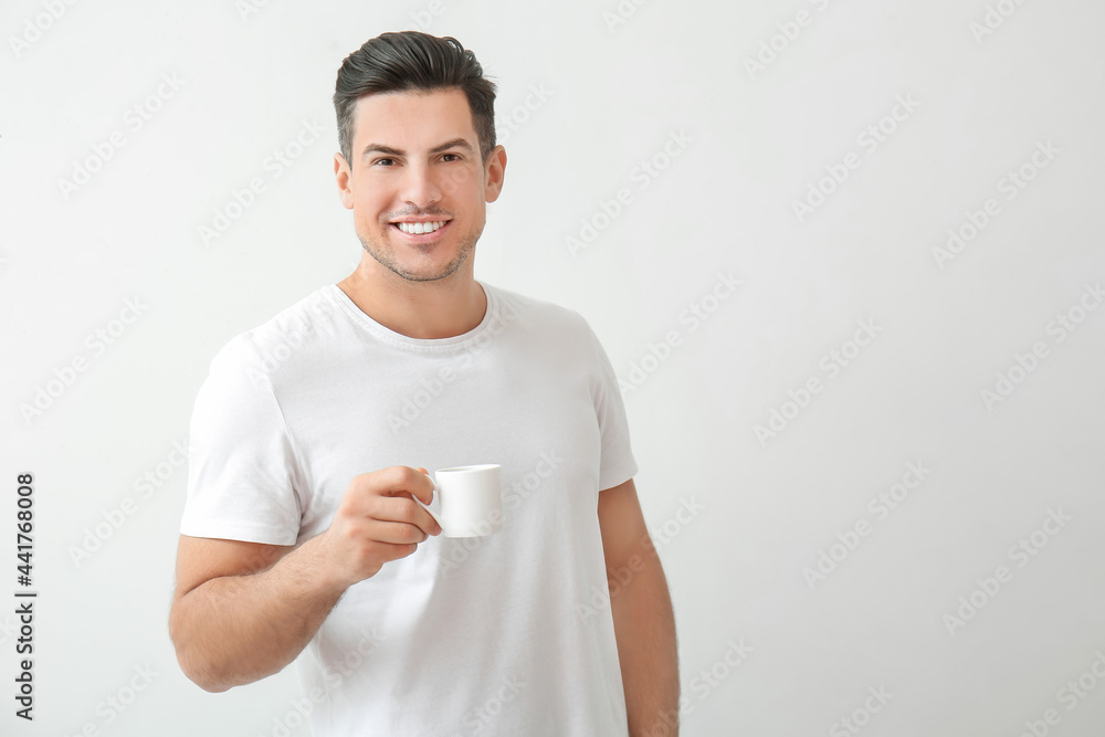 Handsome young man drinking coffee on light background